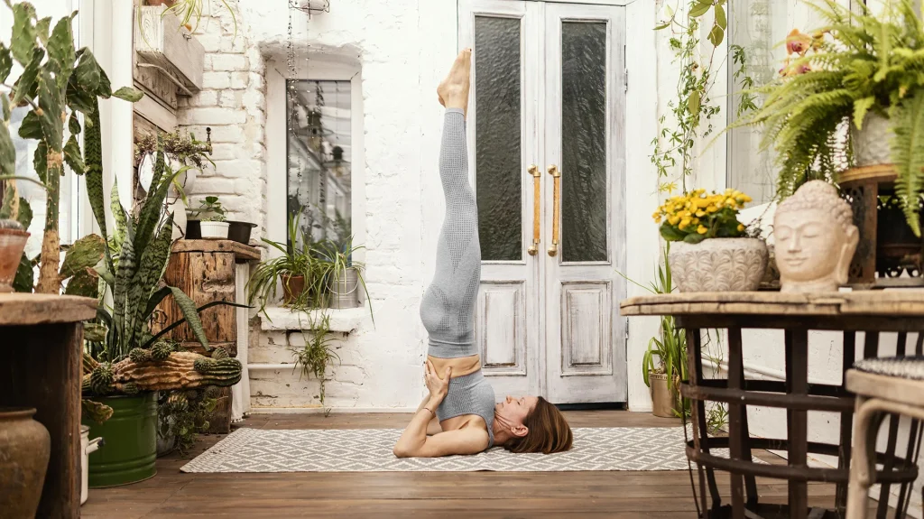 Ragazza che fa yoga in casa circondata da piante