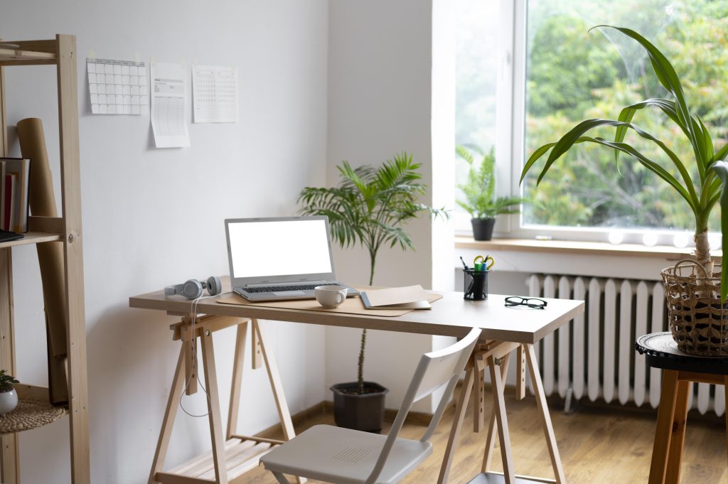 arredamento home office di stile moderno e minimal. scrivani con sedia reclinabile in plastica al centro dell'immagine, sopra la scrivania un PC, una tazza di the, cuffie, un paio di occhiali e un portamatite. diverse piante sulla scena e mobili in legno naturale.