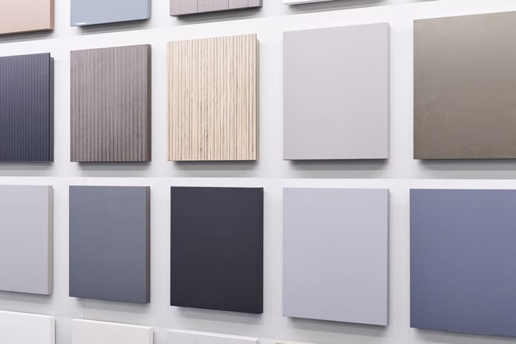 Esposizione a parete di campioni per le finiture dei mobili. I pannelli presentano diverse texture e colorazioni, alternando superfici lisce in laccato opaco dai toni neutri, grigi, antracite e azzurro polvere a finiture materiche in legno con lavorazione cannettata.